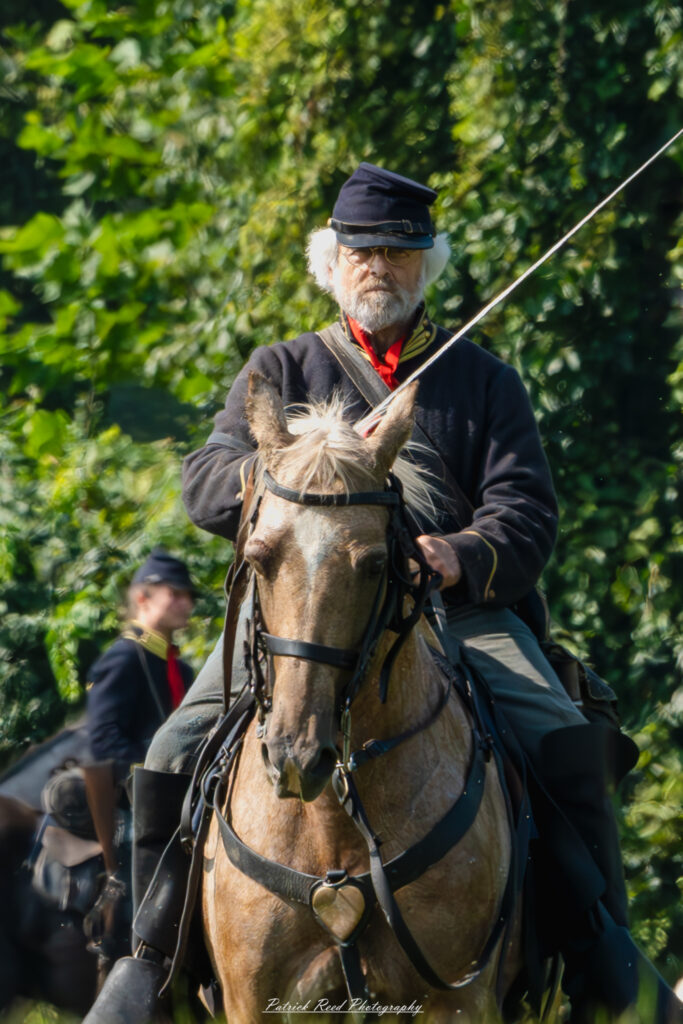An older cavalry soldier on horseback, confidently holding a saber at his side. Dressed in a distinguished military uniform, his weathered face reflects years of experience and dedication. The scene captures his commanding presence and the legacy of service in cavalry traditions.
